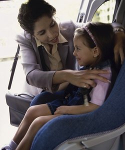 Mother placing her daughter in a car seat