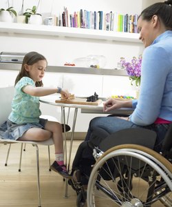 Mother sitting in wheelchair playing chess with daughter (6-8) at table