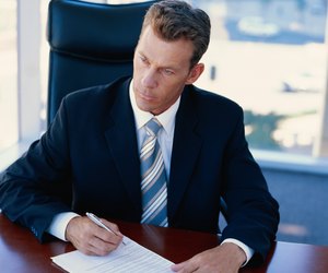 Businessman sitting in office signing document, looking away