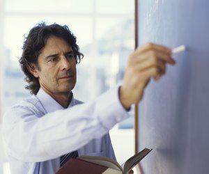 Teacher writing on blackboard and holding book, close up