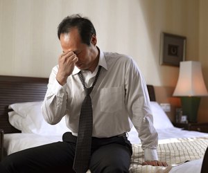 Businessman sitting on side of bed, looking tired.