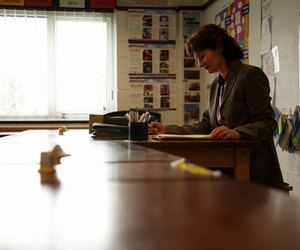 Mature female teacher marking papers at desk in classroom, side view