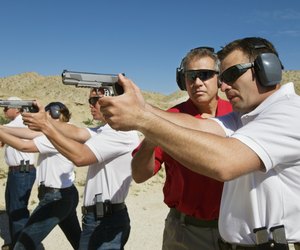 Instructor assisting men aiming hand guns at firing range