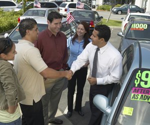 Car salesman selling car to family, shaking young man's hand, smiling