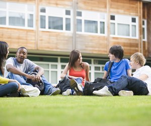 Five students sitting outdoors on lawn talking