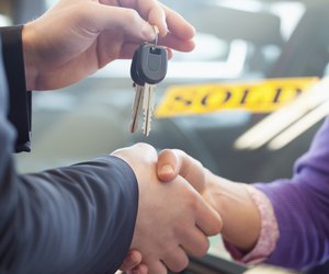 Person shaking hands in front of a sold car