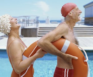 Side view of senior couple poolSide laughing and holding a lifebuoy