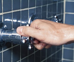 Hand turning water faucet in shower, close-up