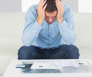 Frustrated casual man sitting on couch paying bills