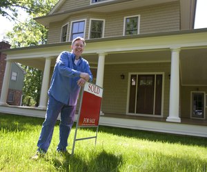 Man standing with for sale sign in front of home