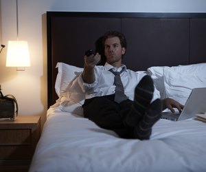 Businessman lying on bed using laptop and remote control