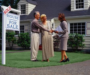 Mature couple and real estate agent standing in front of sold house