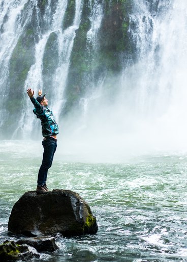Man expressively happy in nature under waterfall