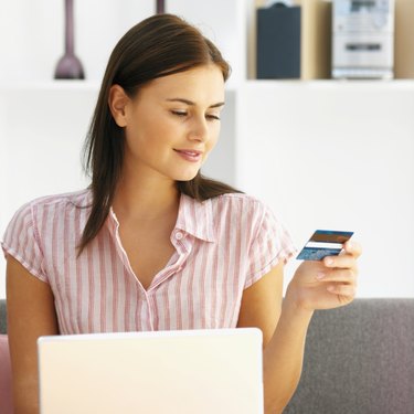 Young woman looking at her a credit card while a laptop