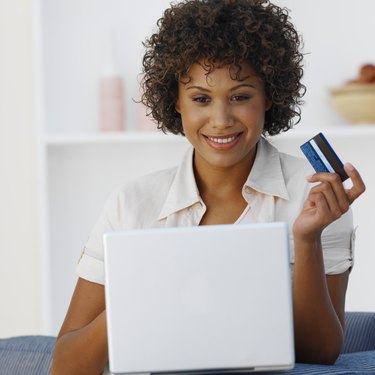 Front view of young woman holding credit card with laptop in front of her