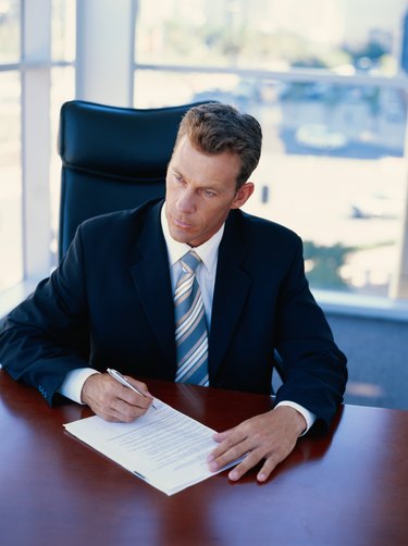 Businessman sitting in office signing document, looking away