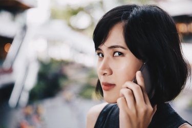 Asian woman looking skeptically at camera while talking on mobile phone