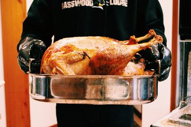 Cook holding roasted turkey in metal pan
