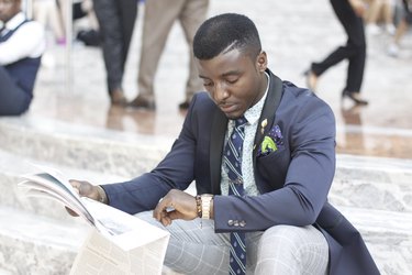Dapper young Black man reading newspaper and checking watch