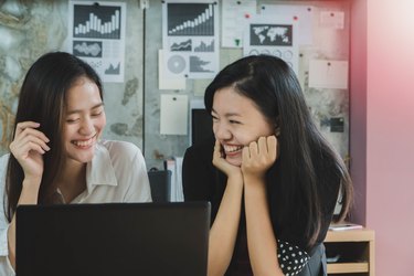Two young Asian women smiling together at a laptop