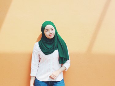 Young Asian hijabi standing against peach-colored wall