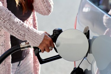 Woman in pink sweater filling up gas tank on white car