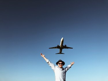 Man doing victory arms with low-flying airplane just above him