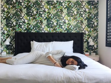 Woman lying on hotel bed in front of tropical wallpaper
