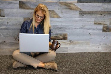 Young blonde woman sitting on floor with laptop and mug