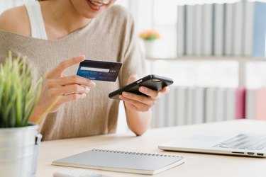 Midsection Of Woman Holding Debit Card While Using Mobile Phone For Online Shopping On Table