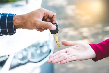 Close up hand male giving a key new car on hand female outside her car. Concept of rent car or buying car.