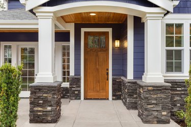 new luxury home exterior detail: patio and front door with arch and columns. Stonework graces the bottom of the columns and house while white columns and archway provide a stately welcome