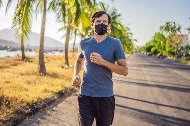 Runner wearing medical mask, Coronavirus pandemic Covid-19. Sport, Active life in quarantine surgical sterilizing face mask protection. Outdoor run on athletics track in Corona Outbreak. Keep your shape during quarantine, pandemic.