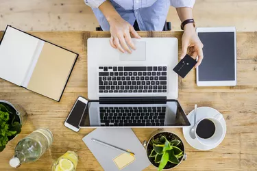 Top view of woman at wooden desk with credit card and laptop