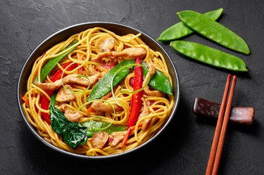 Chicken Lo Mein in black bowl at dark slate background. Lo Mein is Chinese cuisine dish with chicken meat, egg noodles, vegetables and sauces. Chinese Food. Stir Fried Noodles.