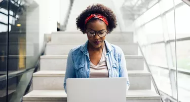 Focused young African student sitting on stairs using a laptop