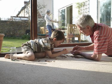 Grandfather and grandson (5-7) counting coins on floor
