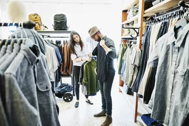 Shopkeeper helping man decide on shirts while shopping in mens clothing boutique