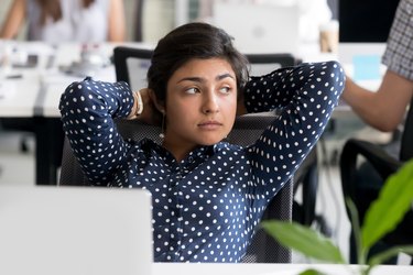Thoughtful Indian female employee leaning back in chair at workplace