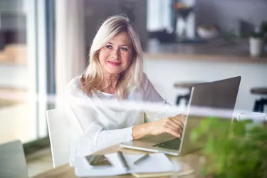 Senior woman with laptop indoors in home office, working.