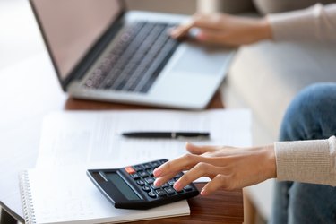 Businesswoman using calculator and laptop for budget cost management, closeup