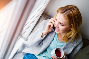 Woman on window sill with smartphone making phone call