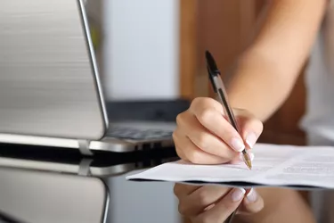 Woman hand writing a contract with a laptop beside