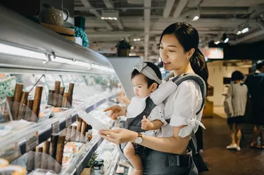 Young Asian mother carrying cute baby girl shopping for fresh organic fish products in a supermarket