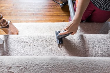 Young woman hand closeup flat top view looking down vacuuming using vacuum on carpet floor inside interior of house living room stairs, steps or staircase, domestic life