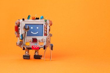Fixing computer concept. Robotic electrician with hand wrenches for repair. Colorful display toy, smile message blue monitor. Service system communication concept. Orange background, copy space