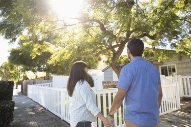 Latinx couple holding hands beneath sunny tree in front yard
