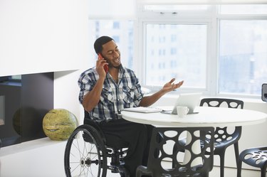 Black businessman in wheelchair talking on cell phone at table