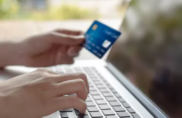 Woman hand holding blue credit card and using a modern laptop, typing and texting