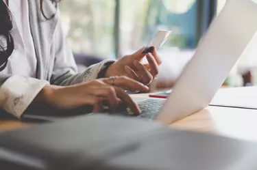 Midsection Of Woman Making Credit Card Payment Over Laptop On Table At Home